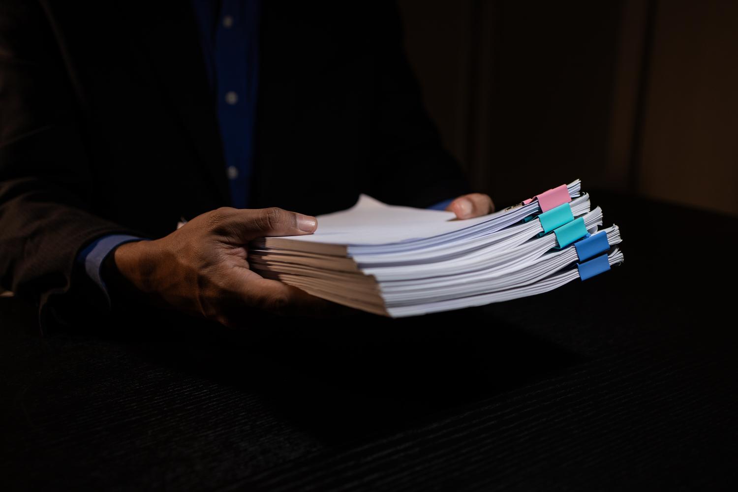 A pile of proof of funds documents held by a hand over a black background