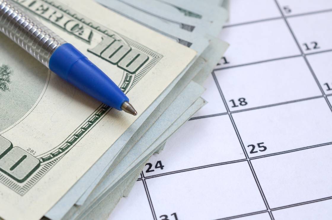 Pen and many hundred US dollar bills on calendar page close up