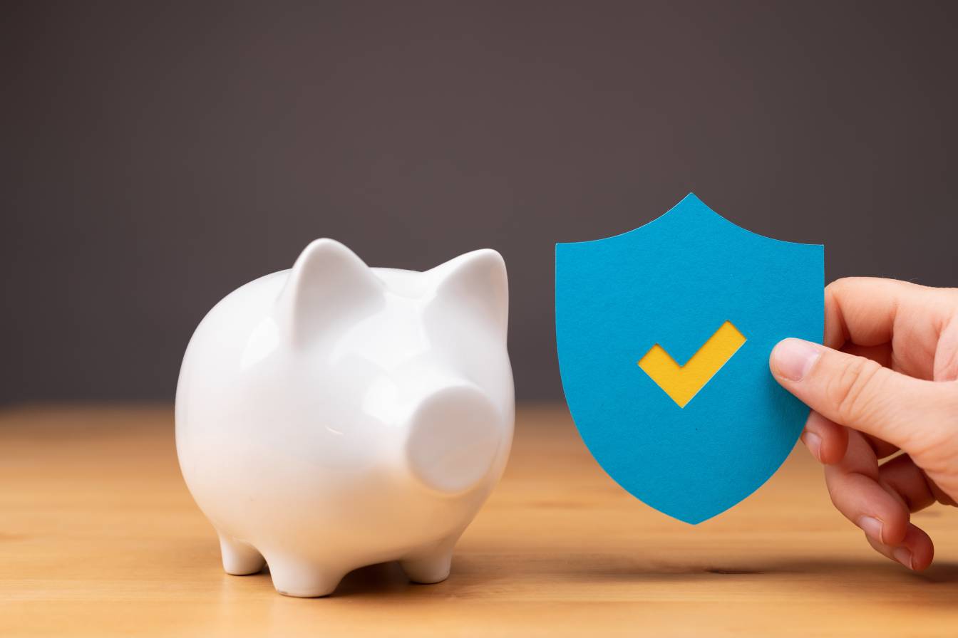 Person holding a blue and yellow secured symbol near a white piggy bank on the table