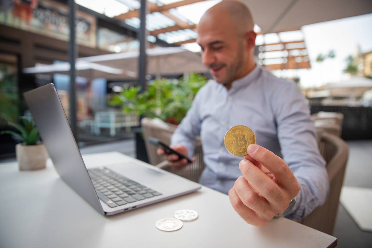 Trader monitors the market with his smartphone while holding a bitcoin coin.