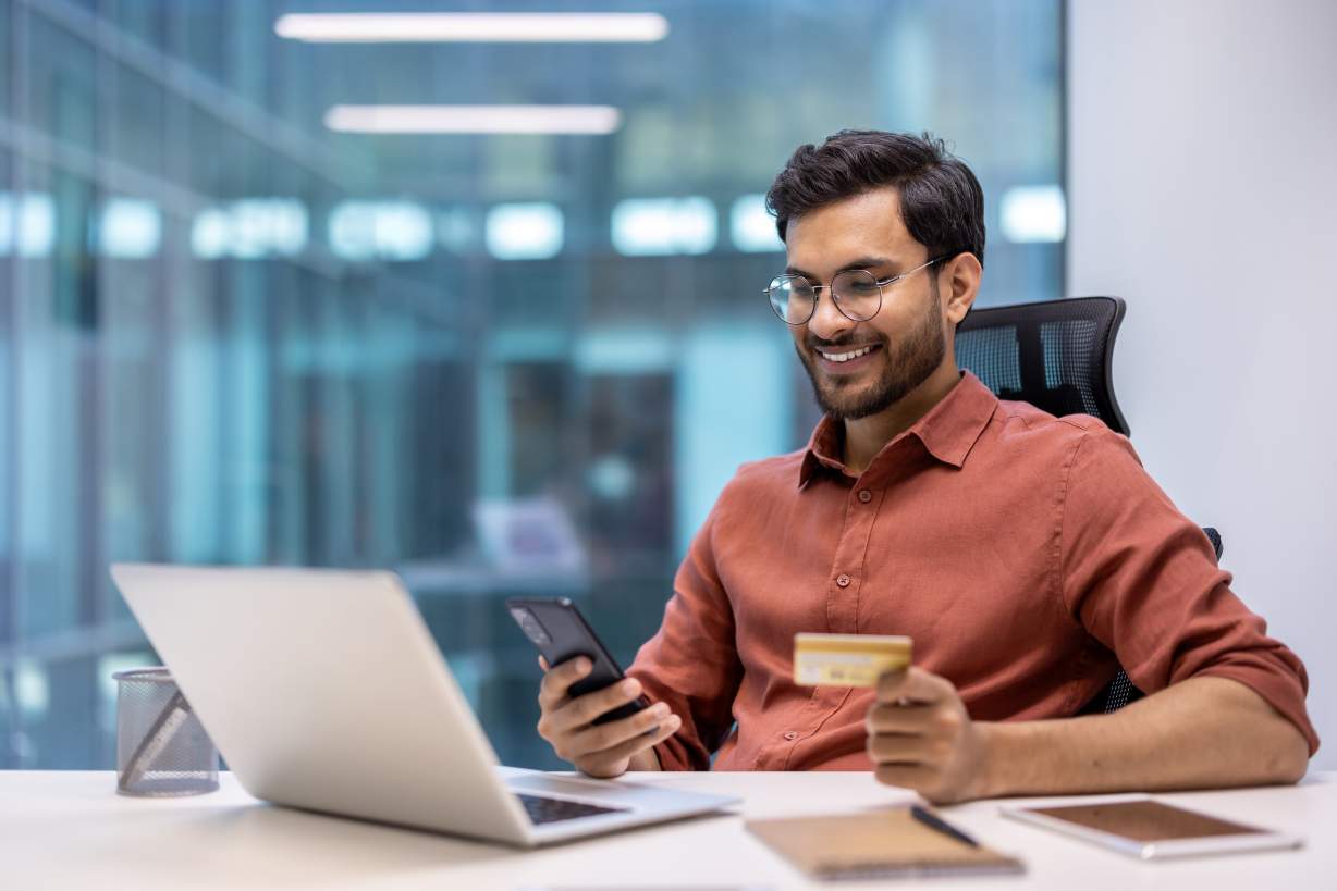 Young businessman using a smartphone and credit card at the office to make an online purchase